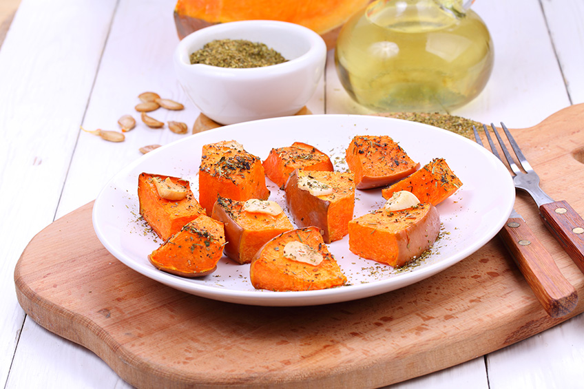 Pieces of butternut squash on a white plate and wooden cutting board.