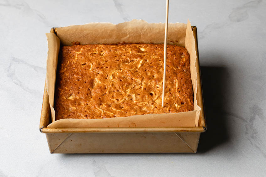 Apple cake being poked with a wooden skewer