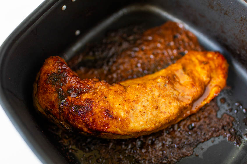 Closeup on flipping pork tenderloin in air fryer basket