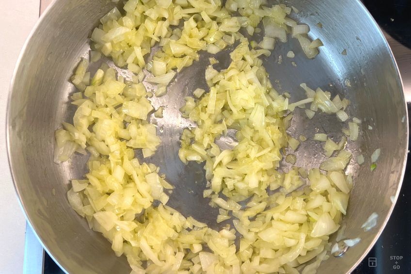 A pot on a stovetop with minced onions and butters frying