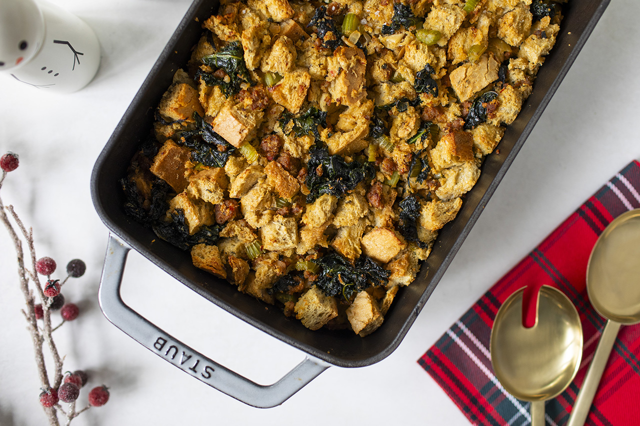 Overhead shot of Marcelle DiLonardo's chorizo and winter greens holiday stuffing, with gold serving utensils and red-patterned napkins