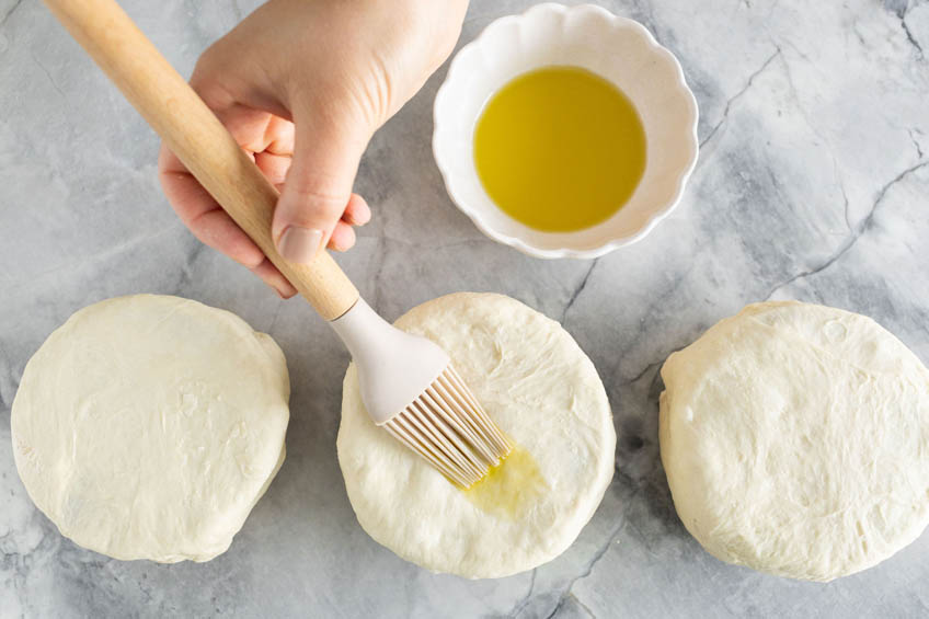 Ramekins topped with dough and being brushed with olive oil