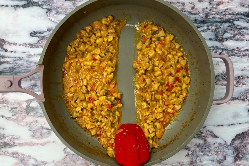 Spatula scraping bottom of skillet, separating chicken mixture