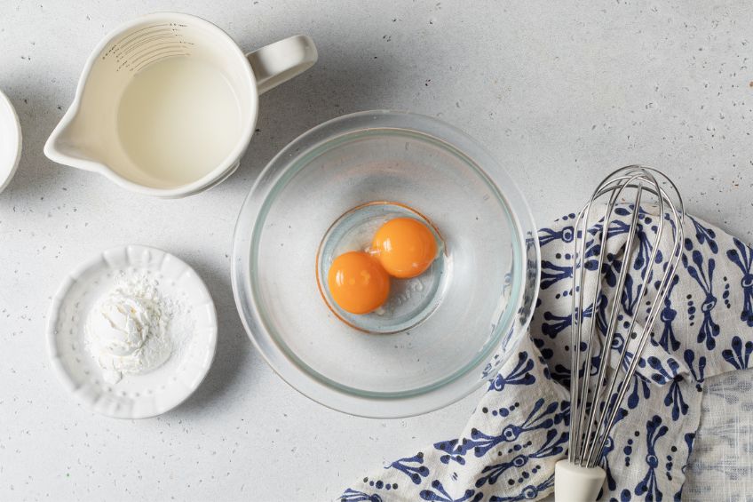 Eggs in a bowl beside a bowl of cornstarch