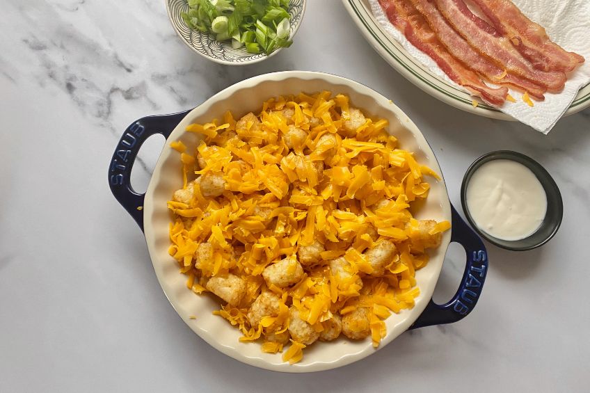 Tater tots in a pie dish topped with grated cheese