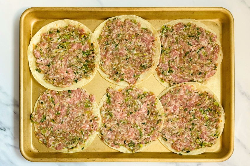 Tortillas on a sheet pan coated in dumpling filling