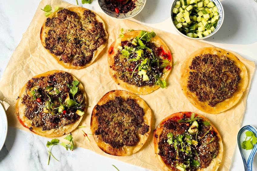 Smash dumpling tacos topped with chili crisp, cucumbers, green onions, cilantro and sesame seeds