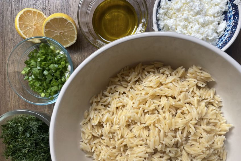 cooked orzo with olive oil, feta, chopped green onion and dill ready to be mixed in a large bowl