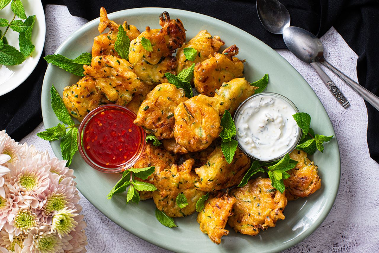 zucchini fritters with harissa honey and mint yogurt arranged on a plate with flowers