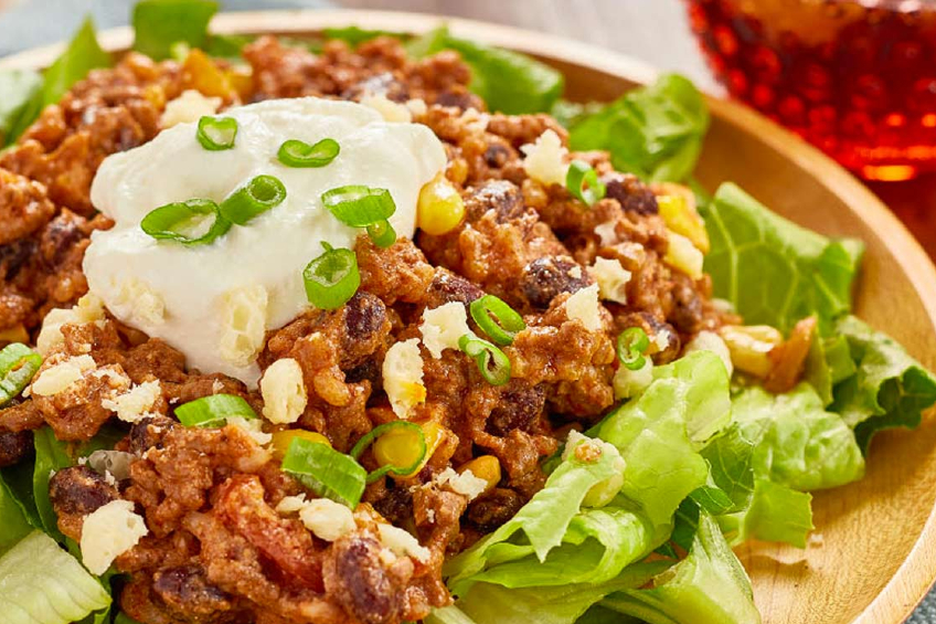 A burrito bowl topped with fresh veggies and a dollop of sour cream