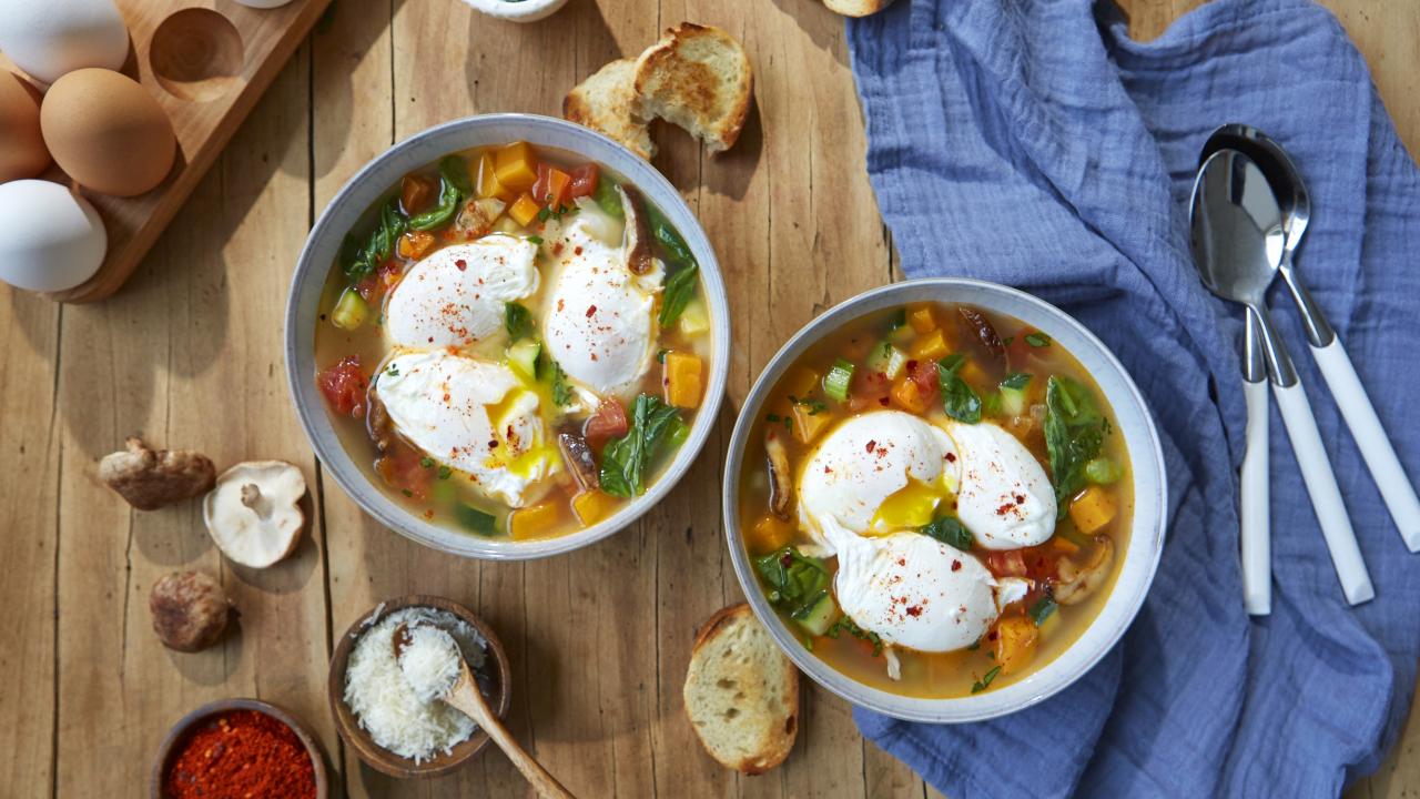 Bowls of vegetable soup on a table with poached eggs on top