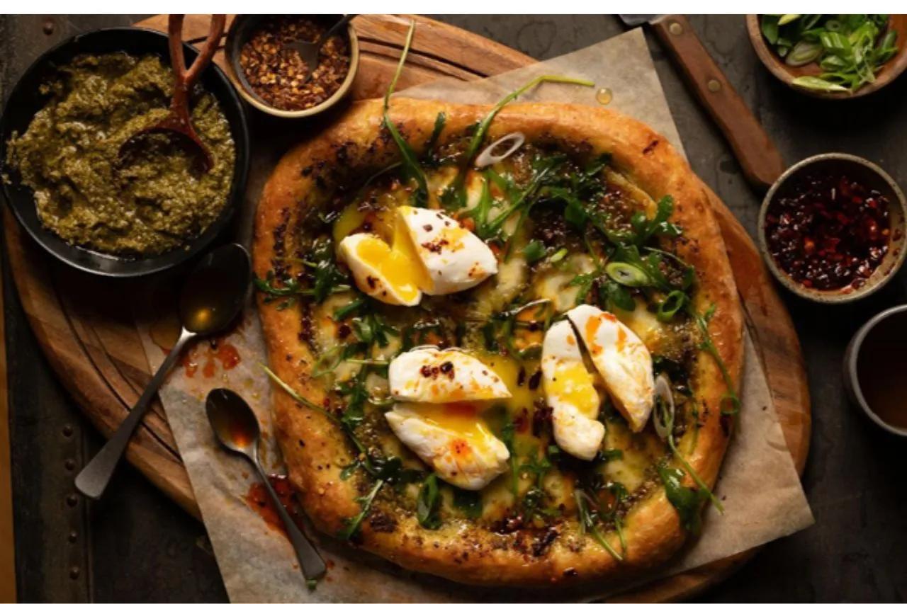 Pesto pizza on a cutting board with poached eggs on top