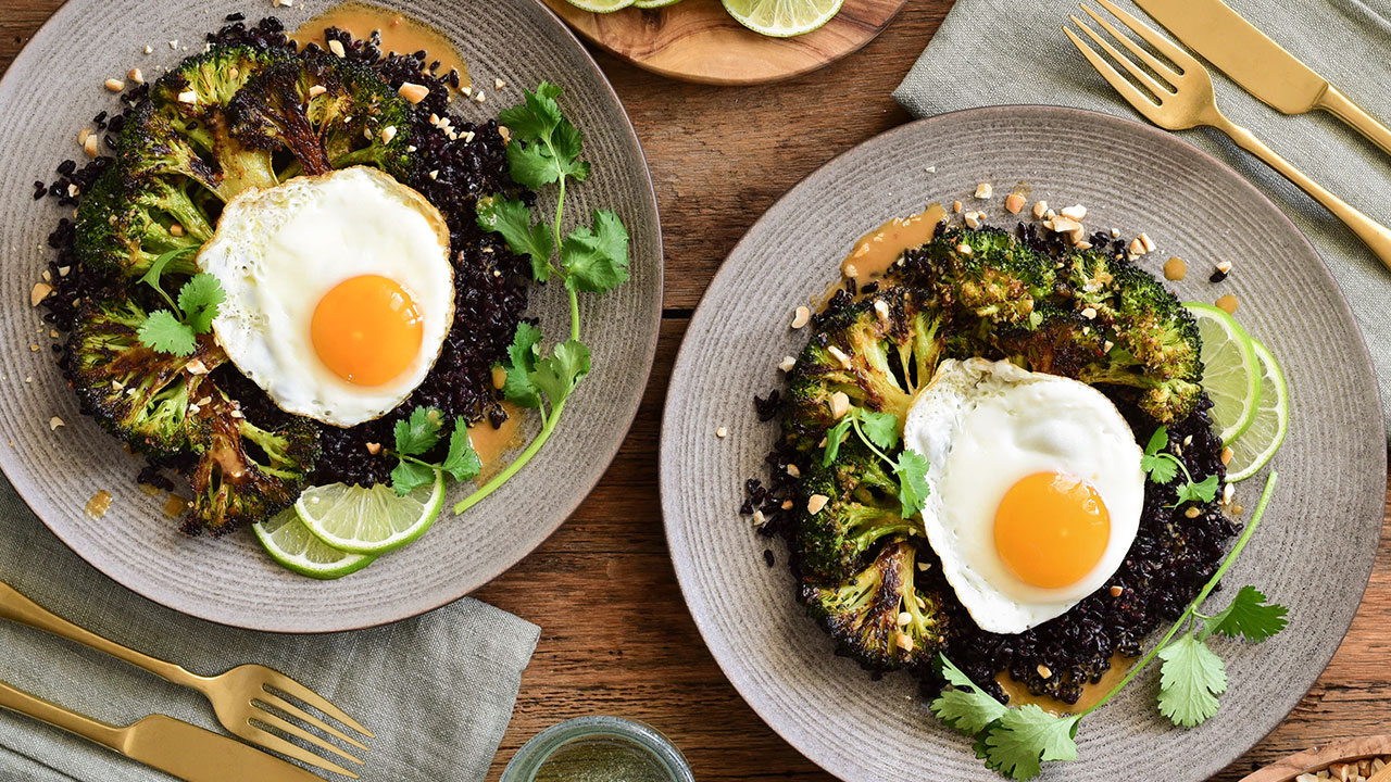 Stir-fried back rice with poached eggs presented on a table on grey plates