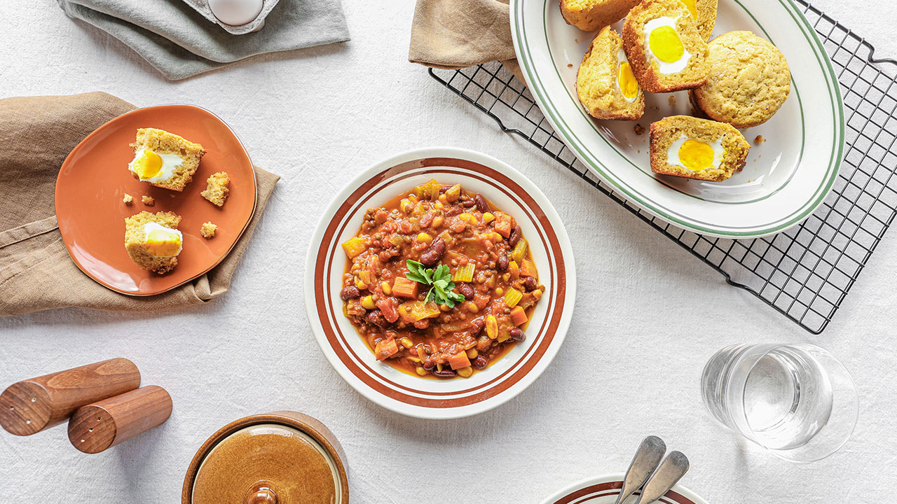 A bowl of chili with egg muffins cut open beside it