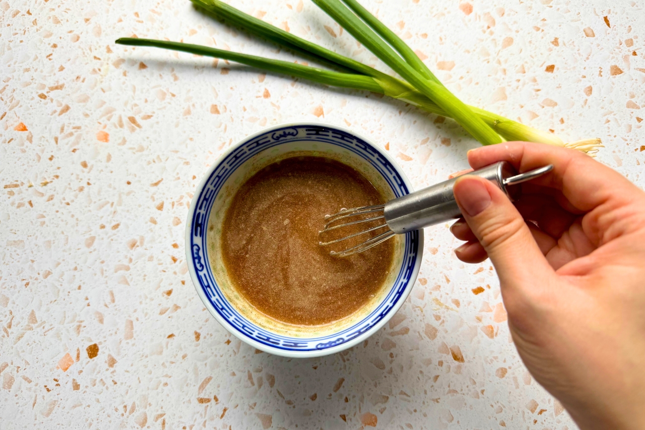 A hand whisking sauce in a bowl