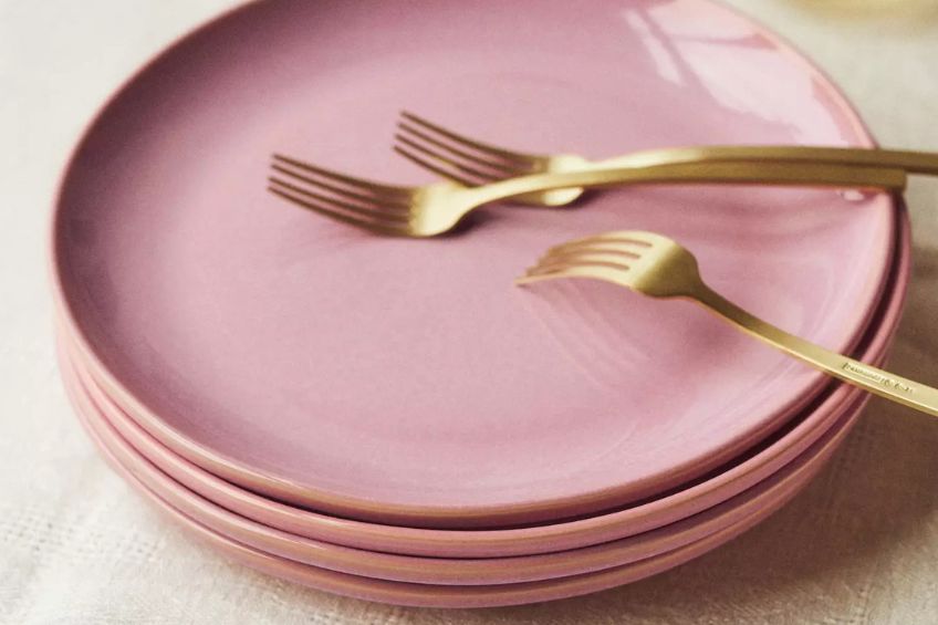 Pink dinnerware plates stacked together with gold forks